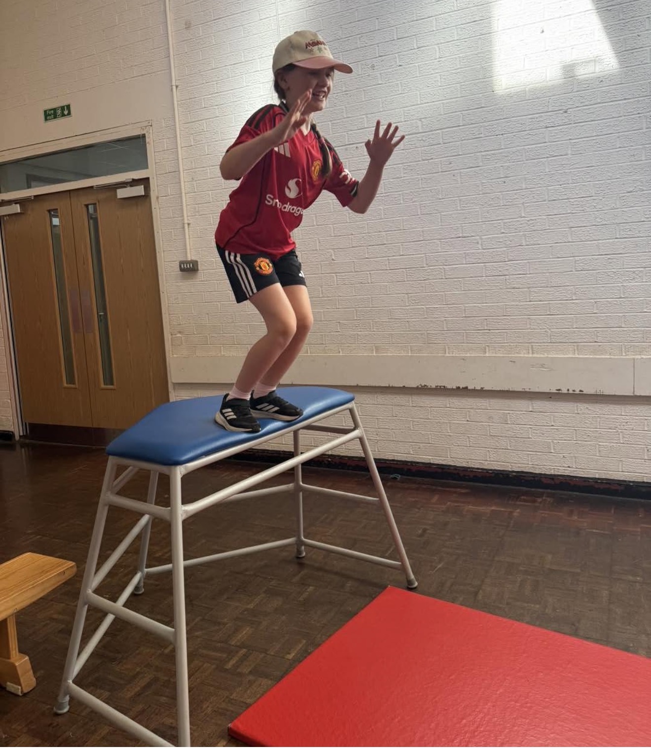 A child jumping from a vaulting box onto a mat in a sports hall