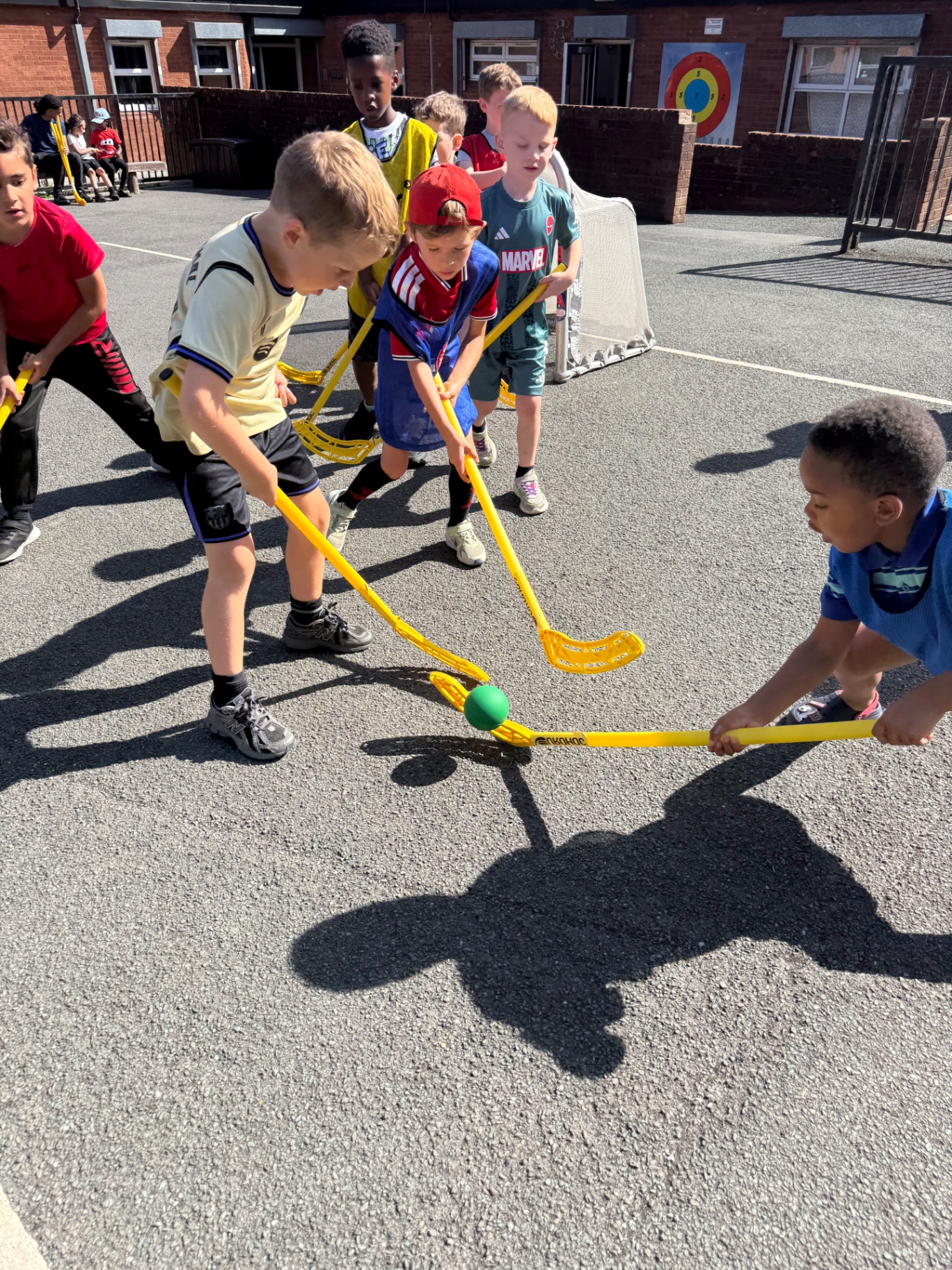 Primary school children playing hockey together in a playground
