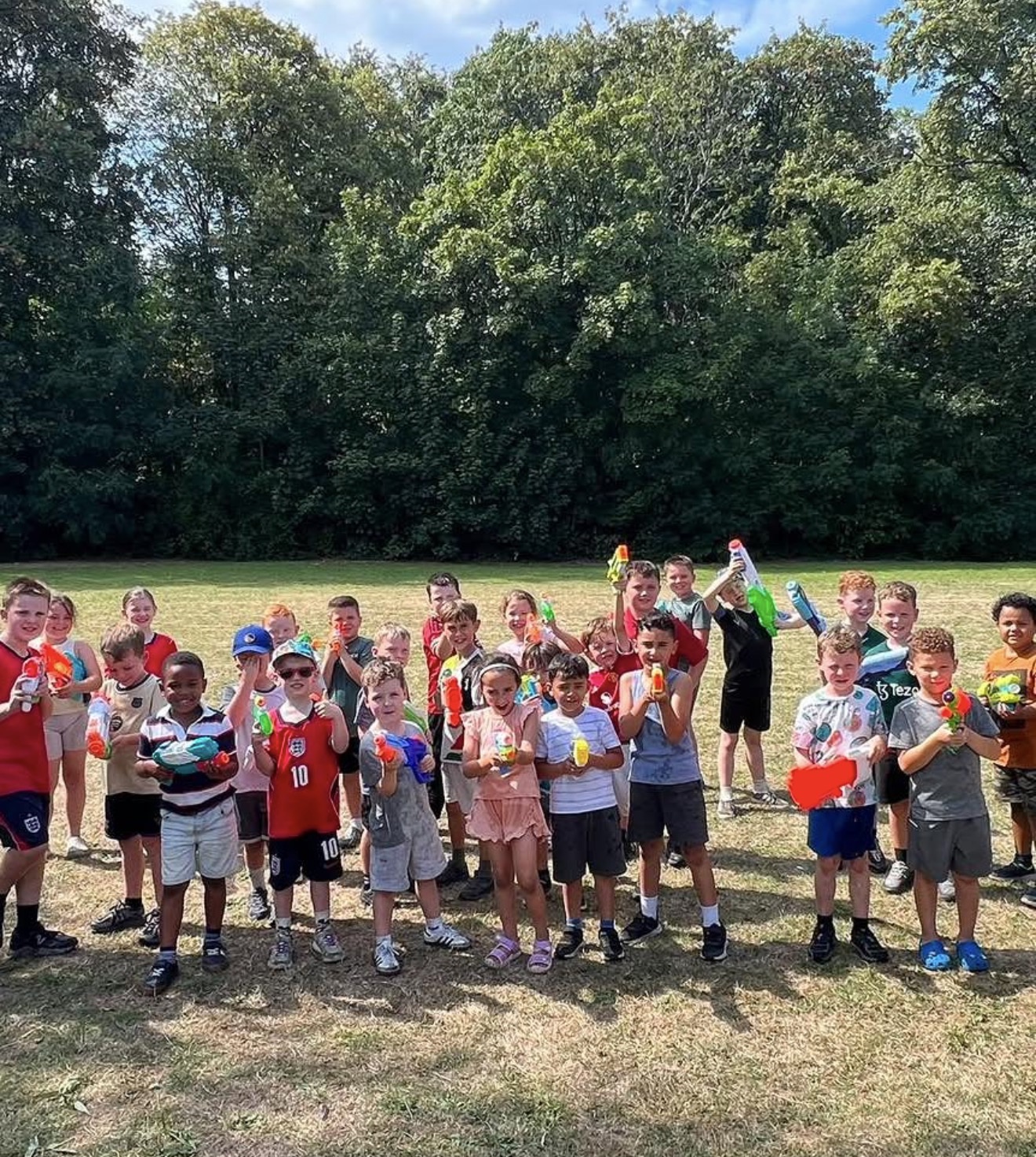 A large group of children with water pistols on a sunny field